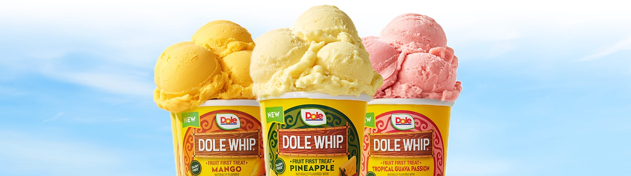 Three cups of Dole<sup>®</sup> Whip in mango, pineapple, and tropical guava passion flavors against sky background